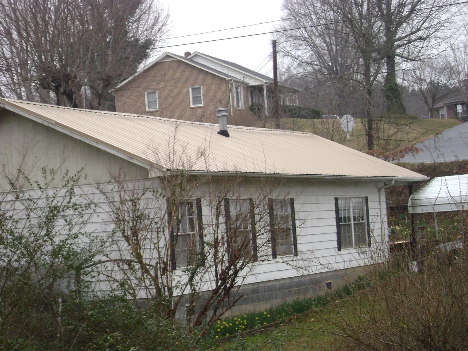 Tan metal roof on a white sided house set into a hillside — Commercial Roofing by Roofing Brothers in Waterville